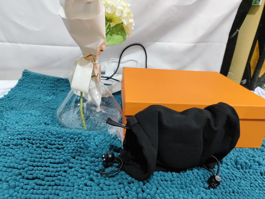 Orange box with a black Black Calming Ear Wrap for Dogs on a blue textured surface, with a white curtain and yellow object in the background.