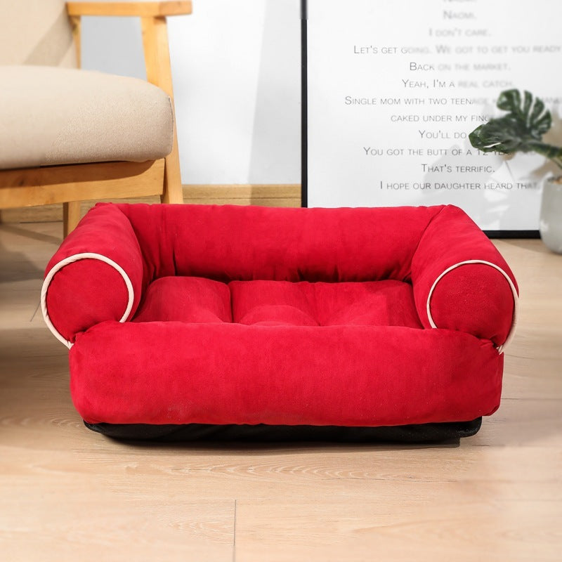 Red pet bed on a wooden floor with a chair and plant in the background