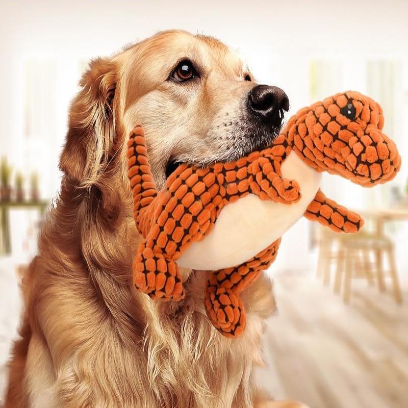 Dog playing with an orange plush toy shaped like a dinosaur