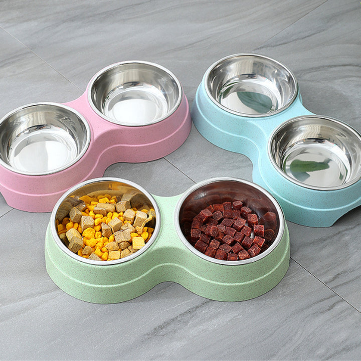 Set of four pet bowls in pink, green, and blue with food inside on a gray surface.