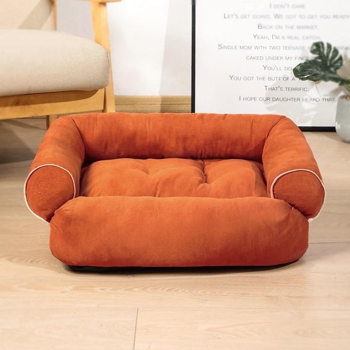 Orange pet bed on a wooden floor with a chair and plant in the background