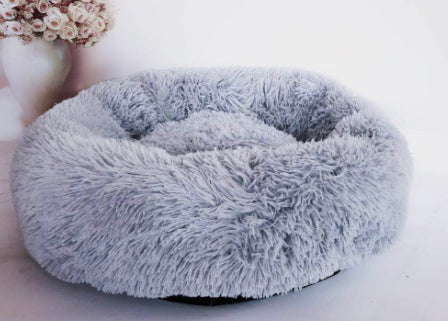Fluffy gray pet bed on a white surface with a blurred background