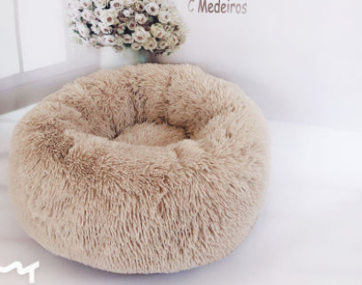 Beige fluffy donut pet bed on a white surface with a blurred background