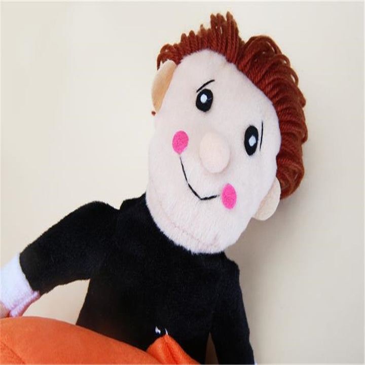 Plush toy with a face, black outfit, and orange pillow on a light background