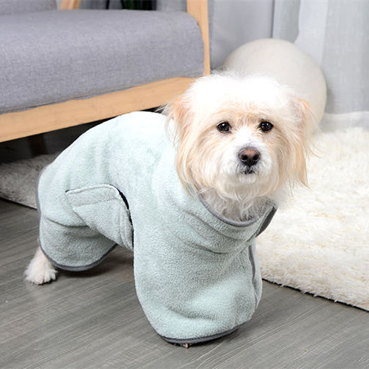 Small dog wearing a light green bathrobe on a wooden floor.
