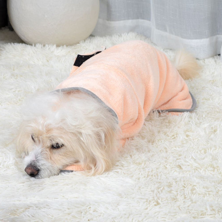 Dog wearing a peach-colored bathrobe lying on a white carpet