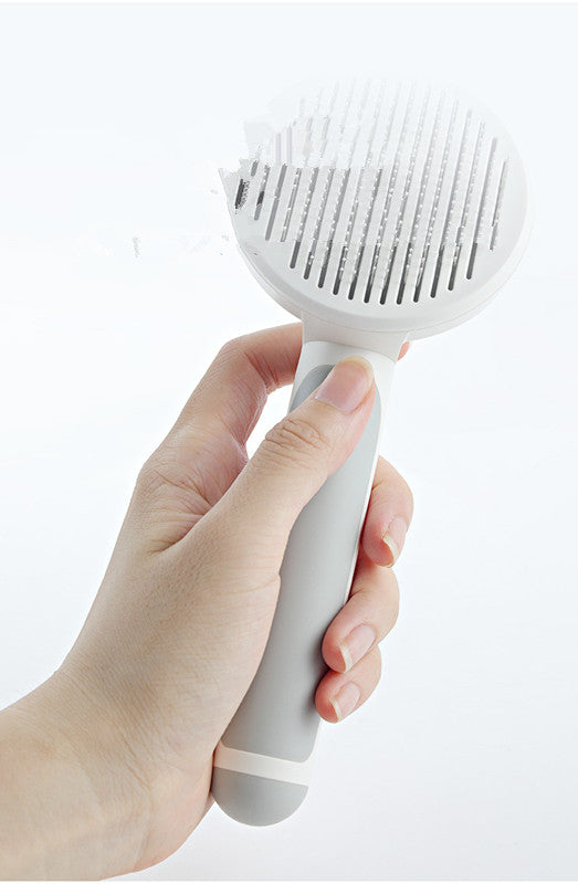 Hand holding a white pet grooming brush against a light gray background