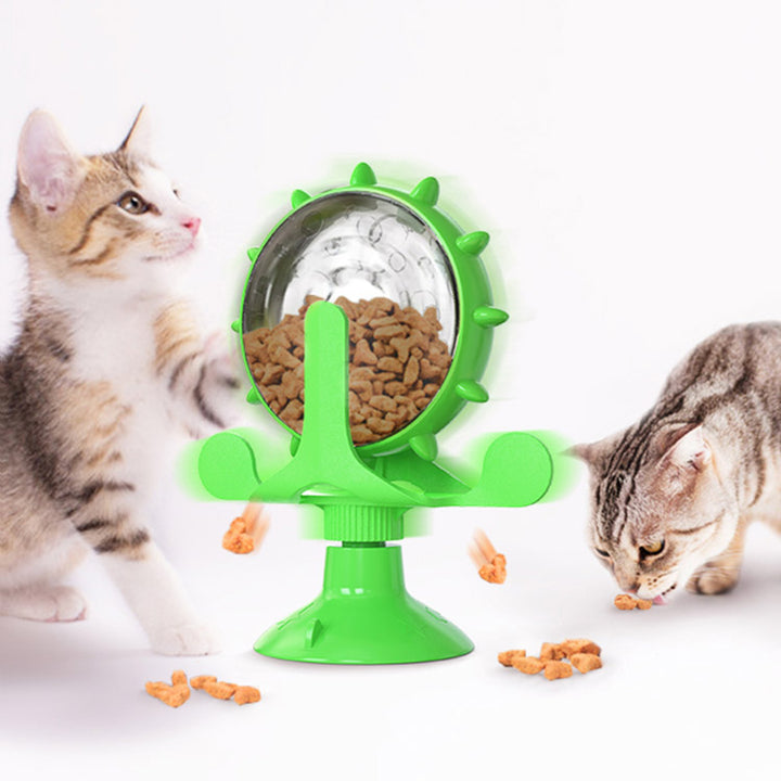 Green interactive pet toy with a spinning wheel containing cat food, with two cats around it.